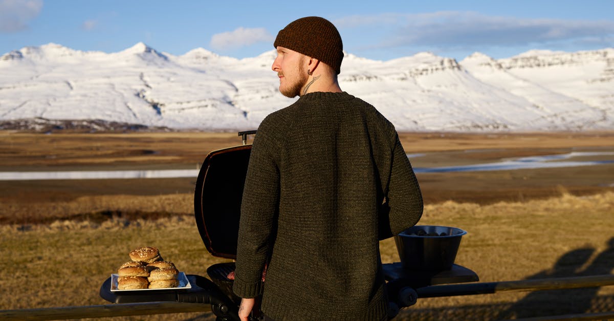 Why do burgers sometimes fall apart on the grill? - Back view of bearded guy in knitted hat and sweater standing opposite snowy covered hills and cooking on grill during trip on nature