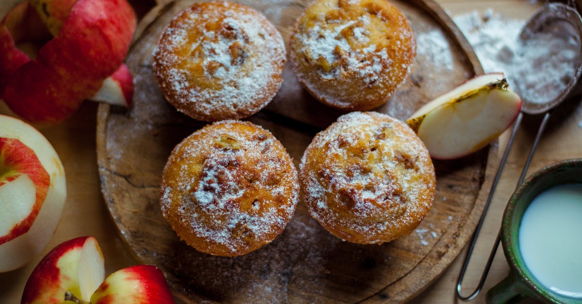 Why do my muffin tops lean? - Top view of delicious baked muffins with powdered sugar placed near cut healthy apples in kitchen