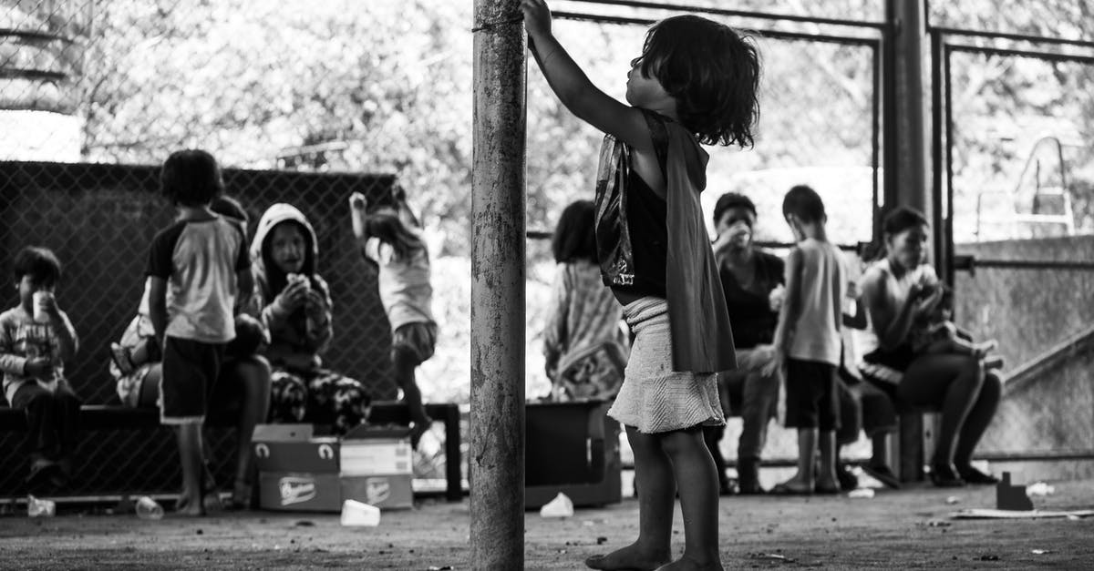 Why do we need to reheat food? - Black and white side view full body of barefoot poor ethnic boy standing near metal pole among people eating food