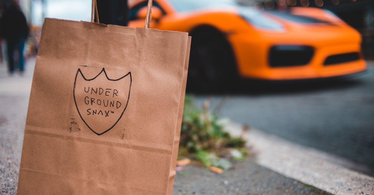 Why does a brown paper bag speed ripening? - Paper shopping bag with inscription placed on asphalt surface near road with driving modern orange sports car