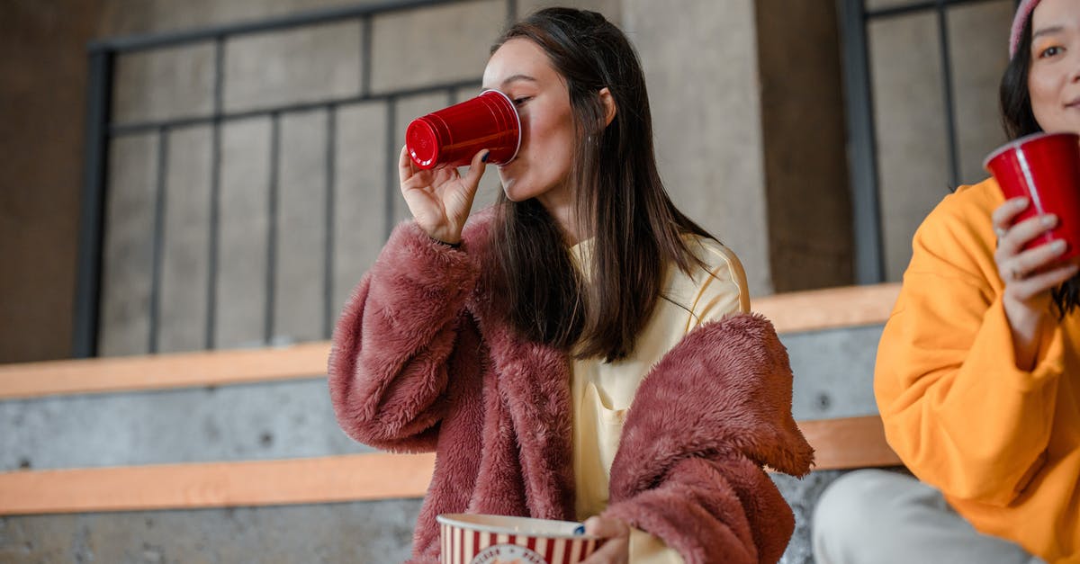 Why does microwave popcorn burn? - Woman in Brown Coat Drinking from Red Ceramic Mug