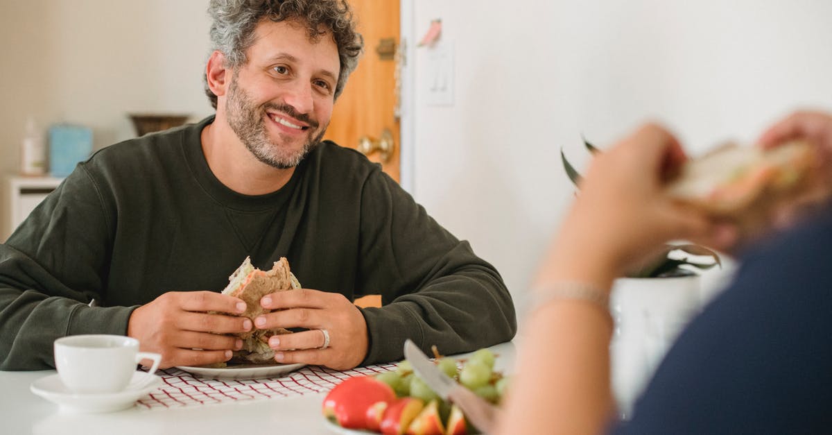 Why does my bread ferment in the middle? - Smiling middle aged guy with beard and gray hair in casual wear eating toast while having breakfast with wife in kitchen