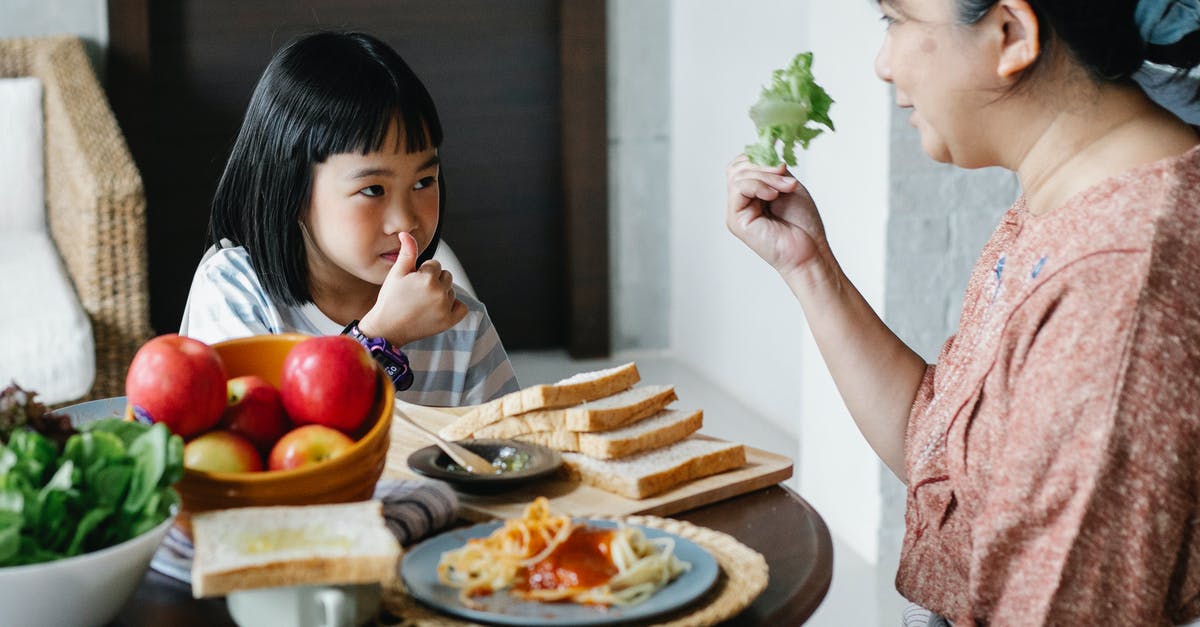 Why does my bread smell like vinegar? - Smiling grandmother showing fresh leaf lettuce while sitting against cute Asian girl showing like gesture and looking at each other