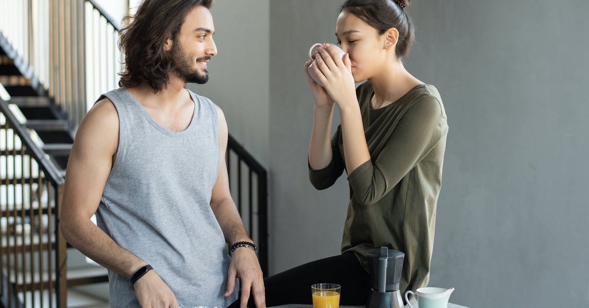 Why does room temperature coffee taste so bad, even to asnomics? - Man in a  Gray Tank Top Standing Beside Woman in Green Top