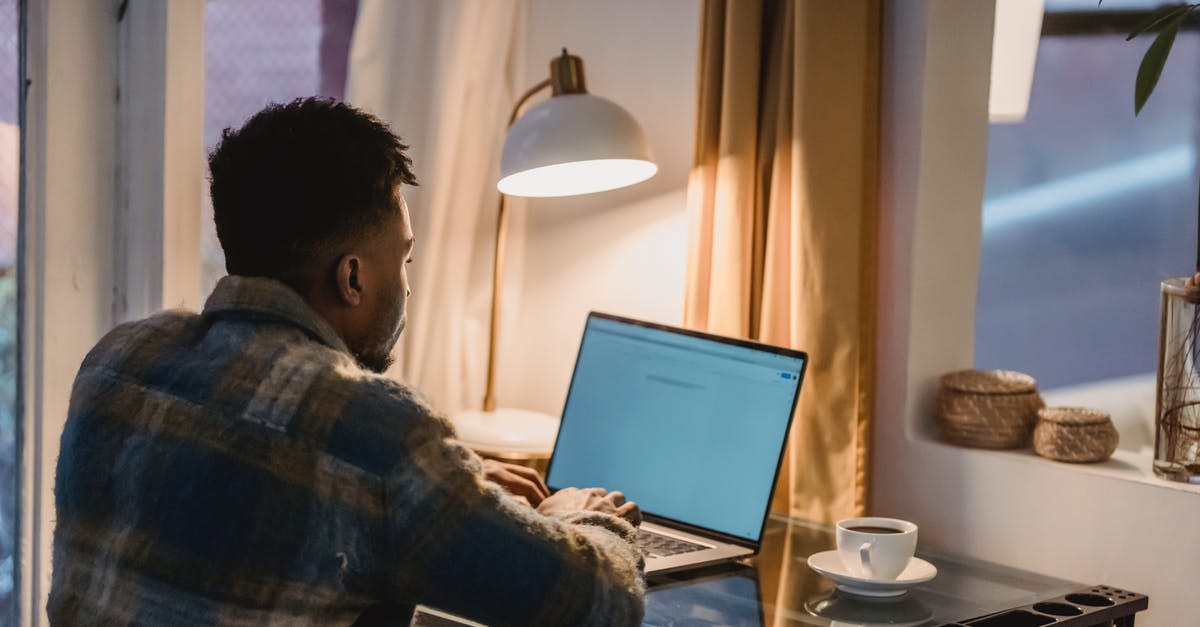 Why does room temperature coffee taste so bad, even to asnomics? - Back view of concentrated African American male typing on keyboard of laptop while sitting at table with cup of coffee and light from lamp