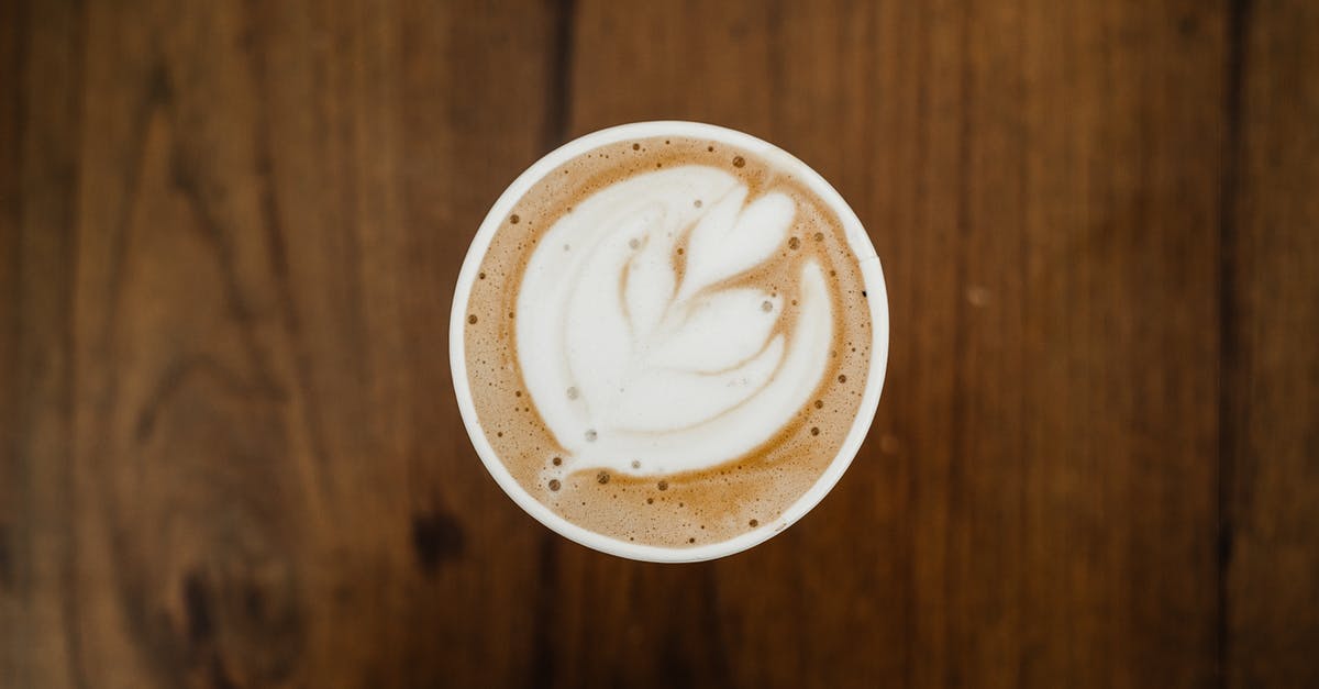 Why does salt prevent soy milk from curdling in hot coffee? - Top view of cup of aromatic cappuccino in ceramic cup with white foam poured in form of plant on brown surface