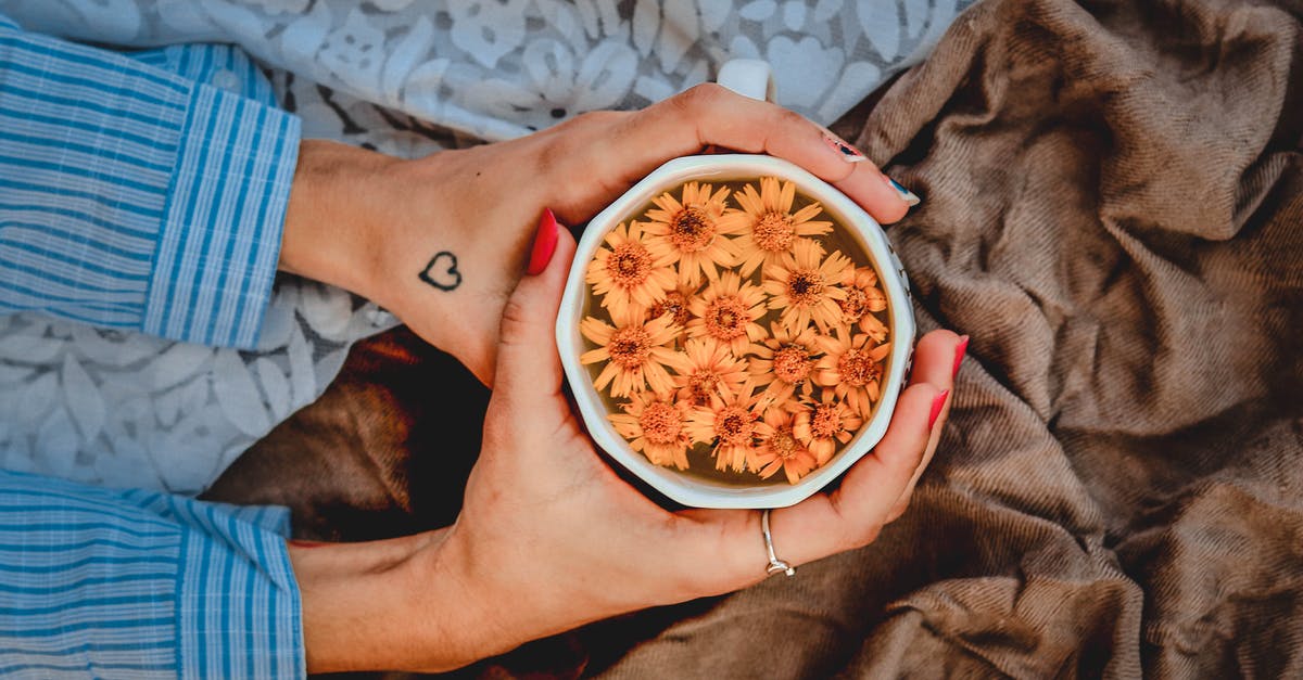 Why does unsweetened tea get colder, faster than sweet tea? - Top view of crop anonymous female warming hands by ceramic mug with hot beverage decorated with fresh flowers