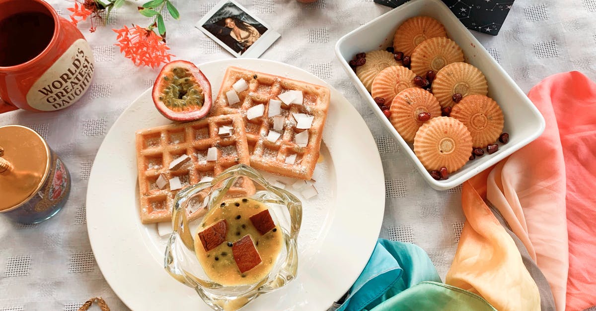Why does waffle dough get dark? - Top view of composition with plate of baked waffles with jam and exotic fruit placed near cookies and colorful neckerchief and mugs