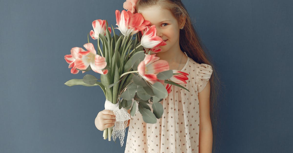 Why is Ginger essence hard to get hold of? - Cheerful little girl with red hairs holding bouquet of red and white flowers and smiling at camera while standing against gray background