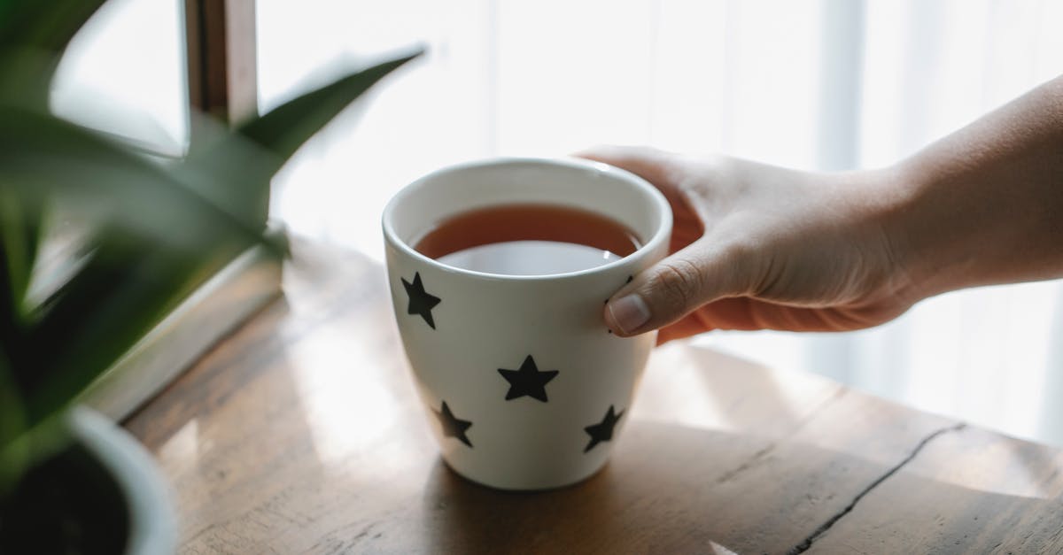 Why is herbal tea brewed at boiling temperature? - High angle of crop faceless person placing mug of hot aromatic delicious tea on wooden table