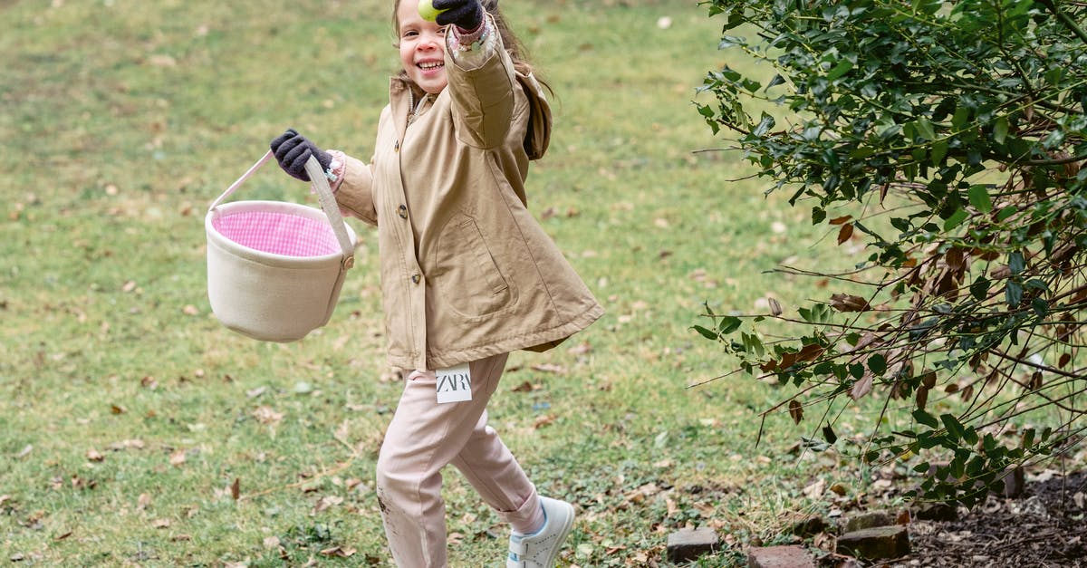 Why is it easier to separate a cold egg? - Full length cheerful girl in warm clothes carrying fabric basket and demonstrating ripe green colored egg or Easter egg in spring park