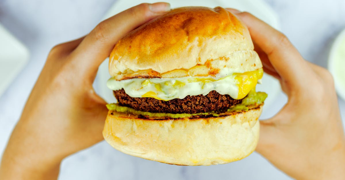 Why is my cheese sauce sweet? - From above of faceless person eating dark brown cutlet between buns in daytime on blurred background