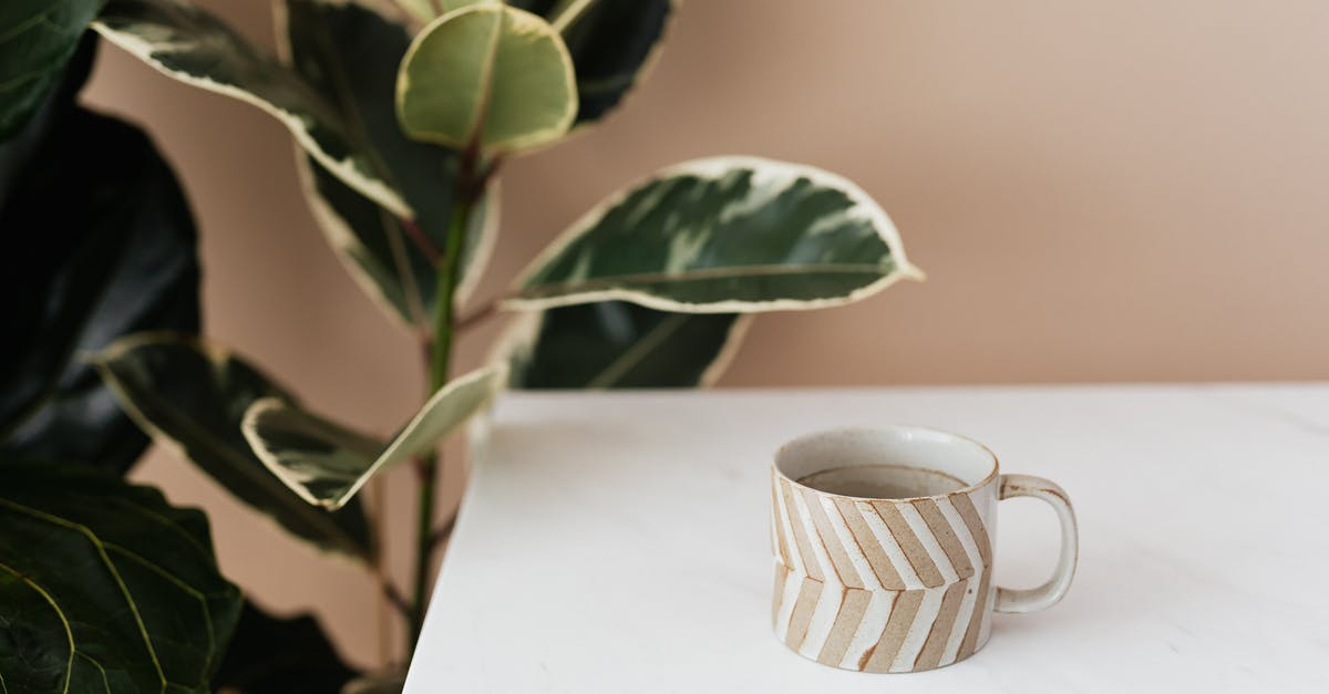 Why is my green tea brown? - Brown and white striped ceramic cup of coffee placed on white marble table near big green ficus plant