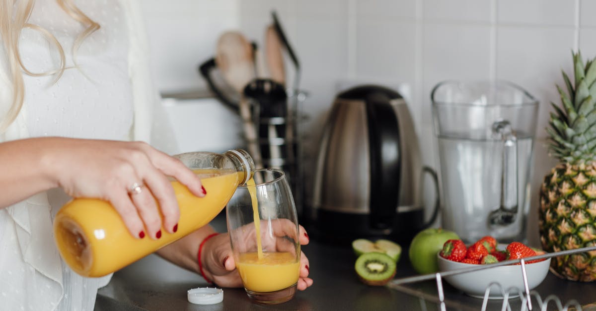 Why is orange juice or apple juice added in a smoothie? - Crop woman poring juice standing near table with fruits