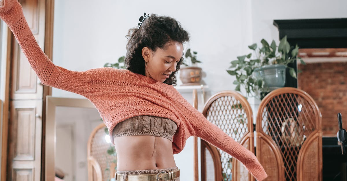 Why is salt sprinkled on top of soft pretzels? - Positive African American female with dark curly hair wearing beige knitted top and leggings with golden belt putting on light orange sweater