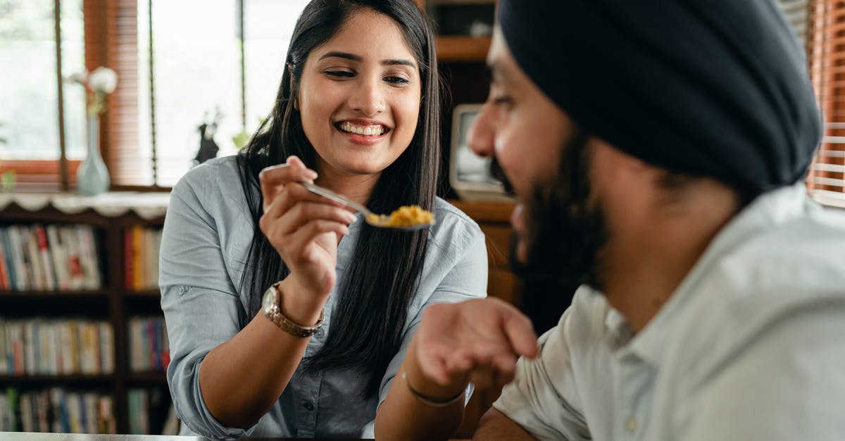 Why is the chicken in Indian food so tender? - Positive young ethnic lady feeding boyfriend with delicious food