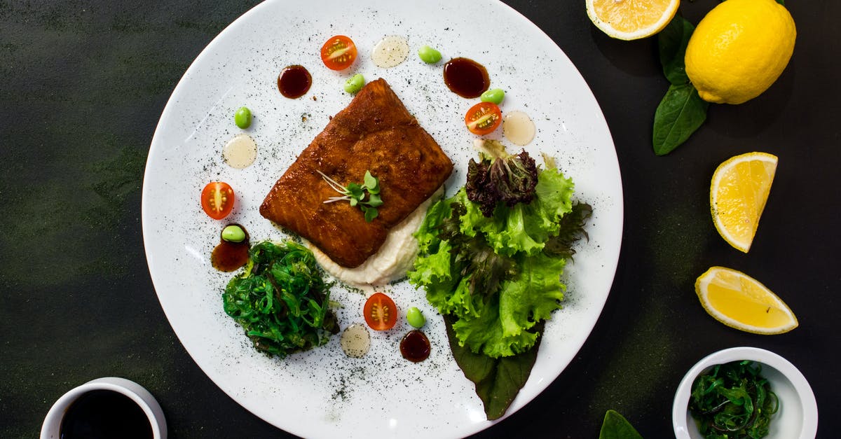 Why not mix meat or poultry with fish? - Top view of delicious fried fish served in white plate with fresh salad and spinach and placed on black table table with lemons tomatoes and sauces