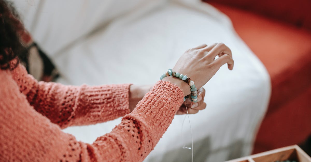 Why put a stone in the soup? - High angle of crop anonymous female designer tying decorative bracelet on wrist made of stones