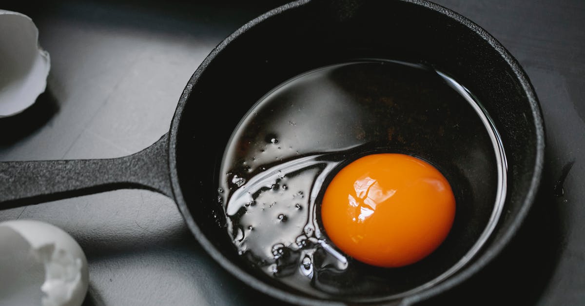 Why reoil a cast-iron pan after usage? - From above of frying pan with uncooked egg yolk and white placed on table near scattered shells in kitchen
