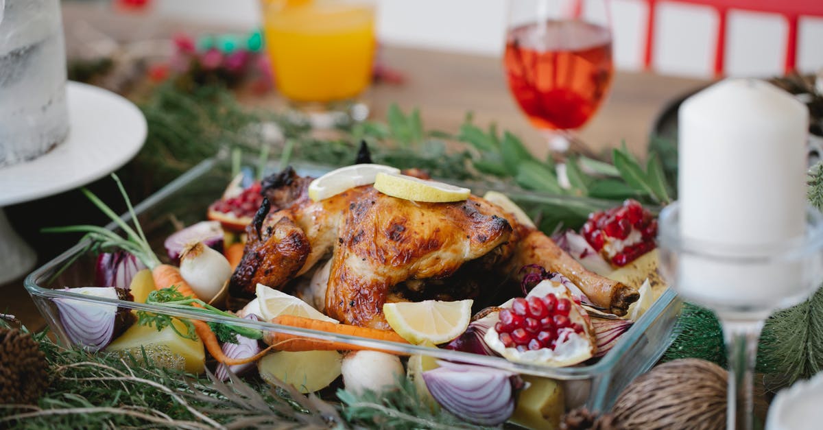 Why season the meat "liberally"? - Roasted chicken on glass form with lemons and pomegranate and carrots on festive decorated table for Christmas celebration with cocktails and candles