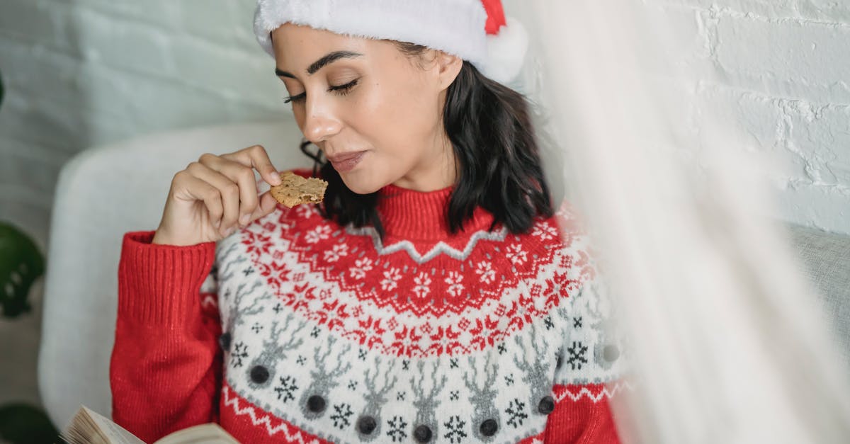 Why should I rest gingerbread dough? - Young female in warm Christmas sweater and hat sitting on sofa while reading interesting book and having gingerbread