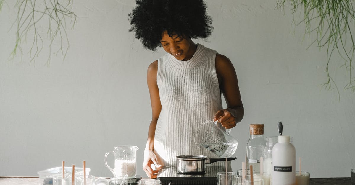 Why should we add alcohol to make extract - Positive African American female artisan pouring liquid in pot while making wax for candles in pot on cooker