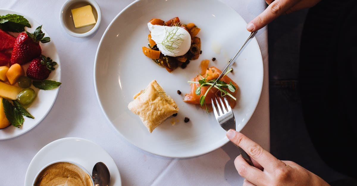 Why should you serve risotto on a hot plate? - Top view of crop anonymous person having tasty appetizing breakfast with fork and knife having hot aromatic coffee