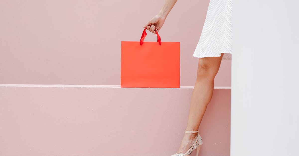 Why spend $150 on a skillet - Crop anonymous stylish female in white dress and high heels carrying red shopping bag against pink wall