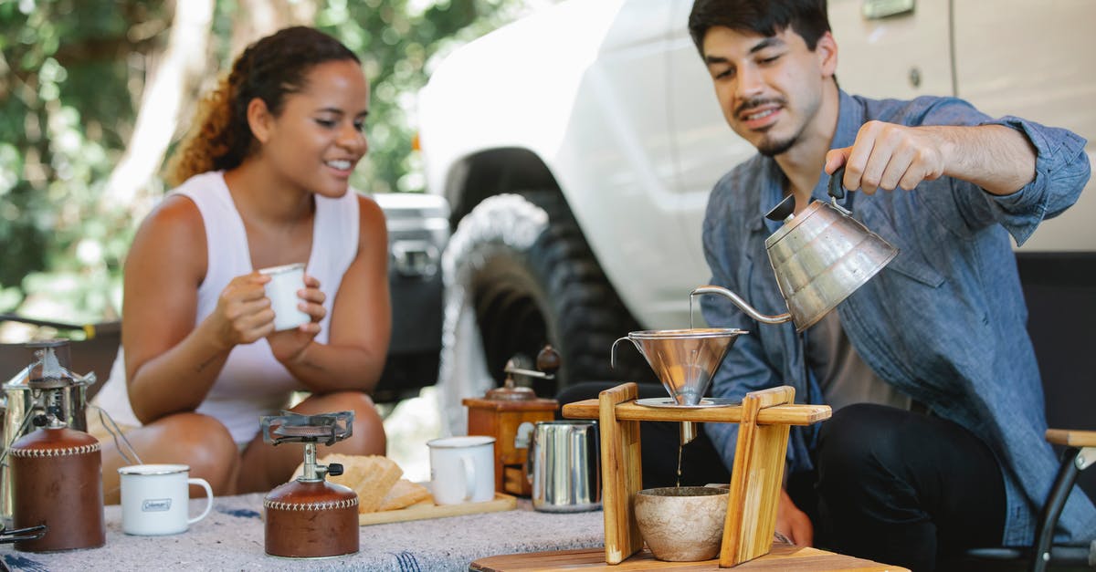 Why use a kettle to heat water? - Cheerful young multiracial couple in casual clothes pouring boiling hot water into pour over filter while having coffee break together in sunny nature