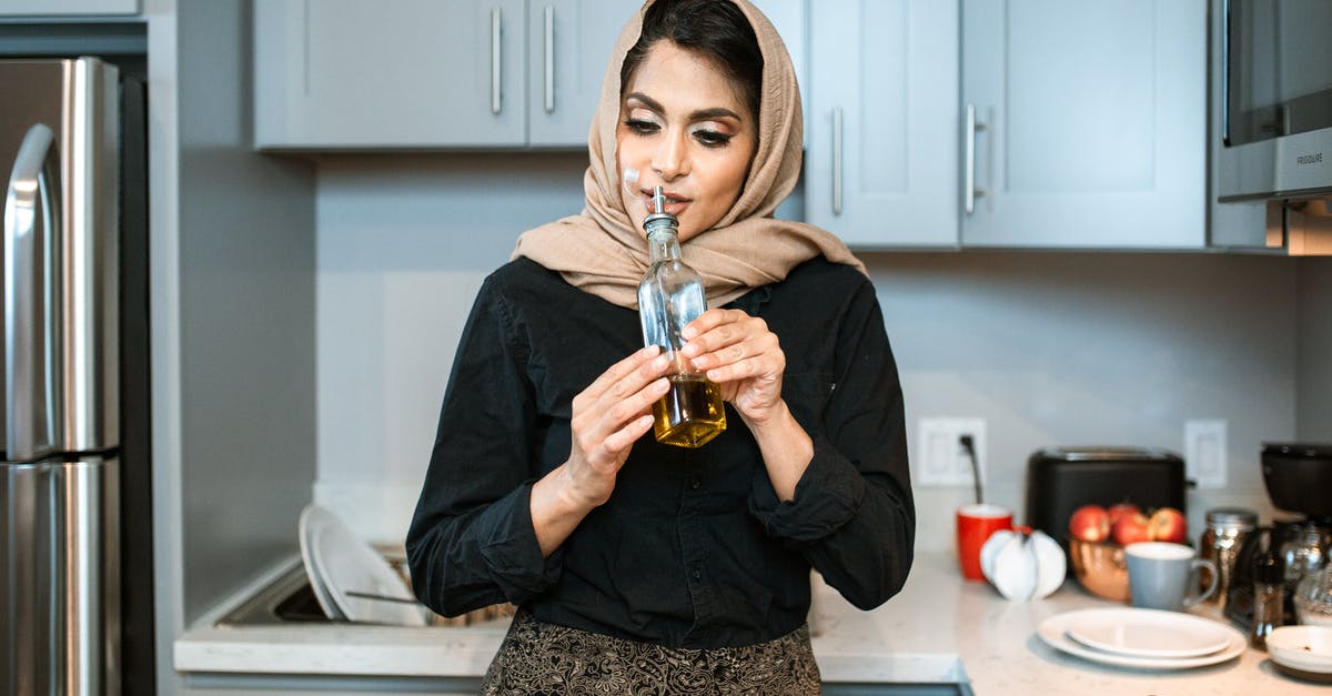 Why would my olive oil smell like chipotle peppers? - Positive stylish ethnic female in headscarf smelling aromatic olive oil in bottle while cooking dinner in contemporary light kitchen