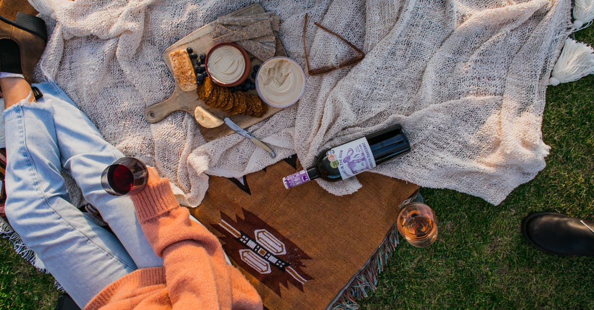 Wine sediment clinging to top of bottle? - Top view of anonymous female with glass of wine sitting on plaid with food while having picnic on grassy lawn