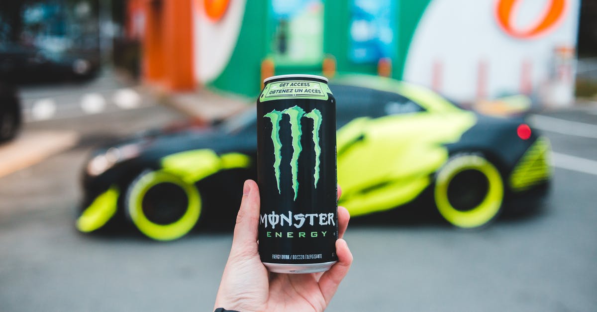 With what can you maximise energy from an induction stove? - Unrecognizable person holding can of power drink while standing on parking lot near sport car