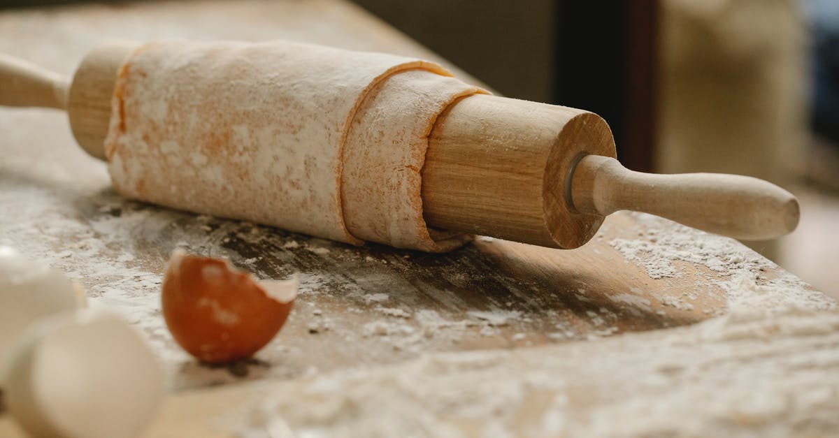 Won't fresh pasta sheets in lasagna overcook? - Rolling pin wrapped with uncooked sheet of dough placed on wooden table sprinkled with flour near eggshells in kitchen on blurred background