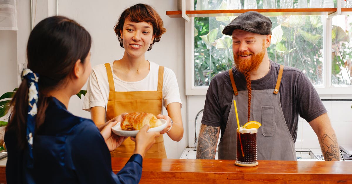 Would a fruit cocktail flavoured cake work? - Cheerful female worker passing delicious puff to unrecognizable partner above counter near smiling tattooed man