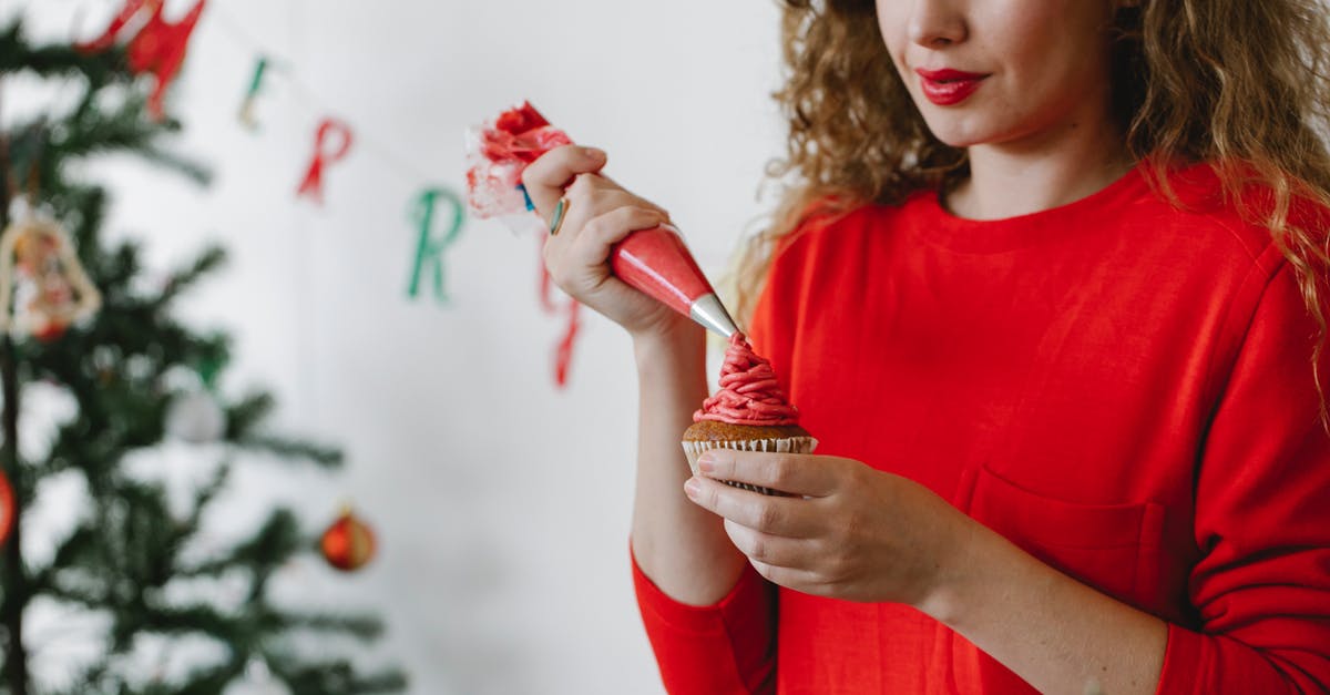 Xmas Pudding put in microwave by mistake for 5 minutes - Concentrated young lady in red sweater piping red cream on cupcake with pastry bag in light room with white wall and decorated Christmas tree